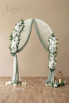 a wedding arch decorated with white flowers and greenery on the floor next to candles