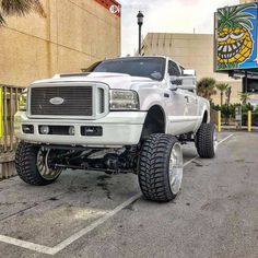 a white truck parked in front of a building with large tires on it's tires