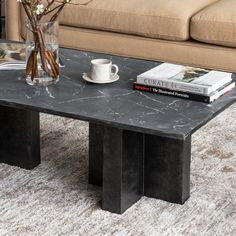 a marble coffee table with two books on it and a vase full of flowers next to it