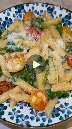 a pasta dish with tomatoes, spinach and parmesan cheese on a blue and white plate