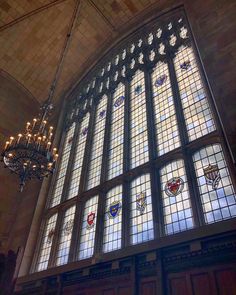 a chandelier hanging from the ceiling in front of a large window with stained glass panels