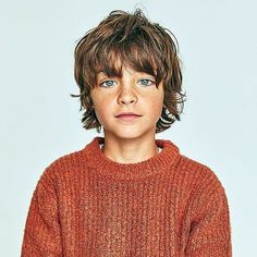 a young boy in an orange sweater is looking at the camera and has his hands on his hips