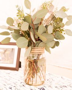 a vase filled with greenery sitting on top of a table next to a framed photo