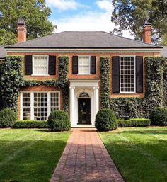 a large brick house with black shutters and white trim on the front door is surrounded by lush green grass