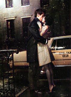 a man and woman standing in the rain next to a taxi cab with their arms around each other