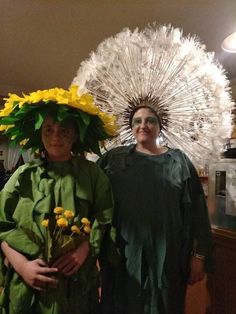 two women dressed in costumes standing next to each other with flowers on their head and one holding a bouquet