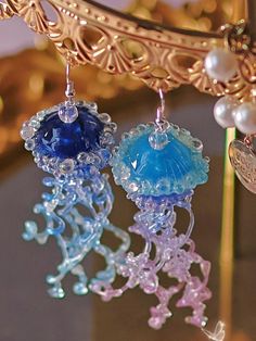 two blue and one pink earrings hanging from a gold chandelier with pearls on it