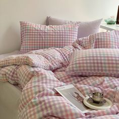 a bed covered in pink and white checkered comforter next to a table with a cup on it