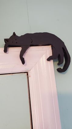 a black cat is sitting on the edge of a pink door frame and it's reflection in the mirror