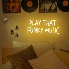 a neon sign that says play that funky music in front of a bed with pillows