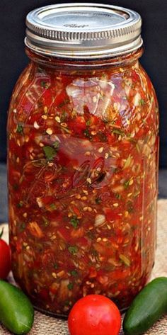 a jar filled with pickles and sauce on top of a table next to tomatoes