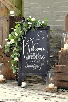 a chalkboard sign with candles and greenery on the table next to some wooden crates