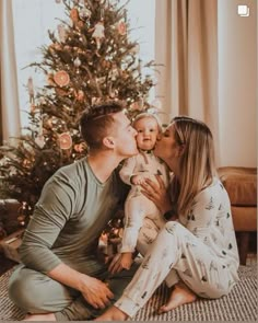 a man and woman kissing their baby in front of a christmas tree