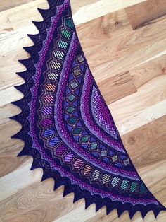 a purple and black crocheted shawl sitting on top of a wooden floor