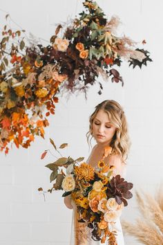 a woman holding a bouquet of flowers in front of a white wall with dry grass