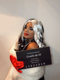 a woman dressed up as cruela de vil holding a sign in front of her face