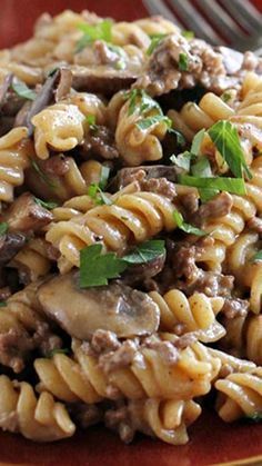 a close up of a plate of food with pasta and meat on it next to a fork