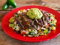 a red plate topped with meat and veggies on top of a wooden table