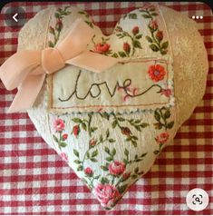 a heart shaped pillow with the word love written on it and a bow at the top