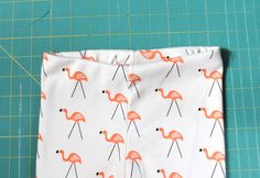 a pair of pink flamingos on white fabric next to a green cutting board with scissors