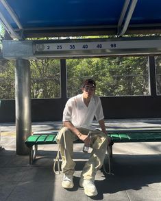 a man sitting on a green bench under a blue awning with trees in the background