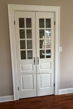 a white double door with glass panels in a room that has hardwood floors and walls