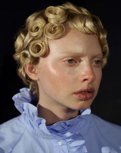 a woman with blonde hair and blue shirt looking at the camera while wearing curly curls