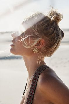 a woman with her hair in a bun and earrings blowing out the wind at the beach