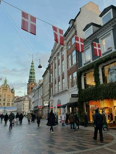 many people are walking down the street in front of some buildings with flags on them