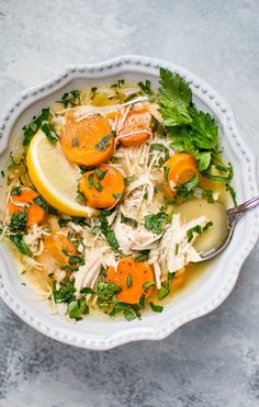 a white bowl filled with soup and garnished with lemons, parsley and carrots