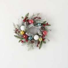 a christmas wreath with ornaments hanging from it's side on a white wall background