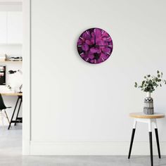 a white room with a purple clock on the wall next to a table and chair