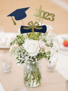 a vase filled with flowers and two graduation decorations on top of a table next to glasses