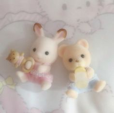 two small toy animals sitting next to each other on a bed