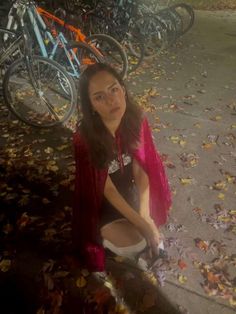 a woman sitting on the ground in front of parked bikes and fallen leaves at night