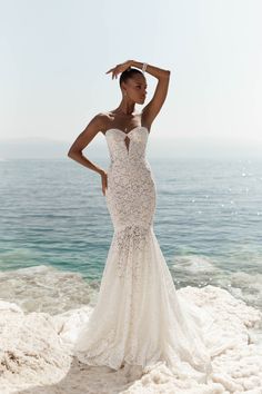 a woman standing on top of a beach next to the ocean wearing a wedding dress