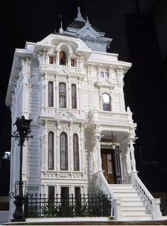 a white doll house with stairs and balconies on the front porch, next to a lamp post