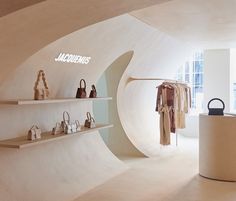 the inside of a clothing store with white walls and shelves filled with handbags, purses and bags