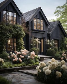 a black house with lots of windows and white flowers in the front yard, surrounded by greenery