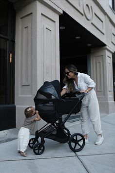 a woman pushing a baby in a stroller on the sidewalk next to a building