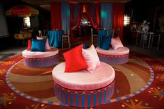 three round couches with red and blue pillows on them in a brightly lit room