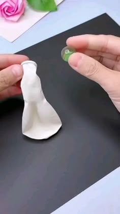 two hands are making a small white vase out of paper and glue on the surface