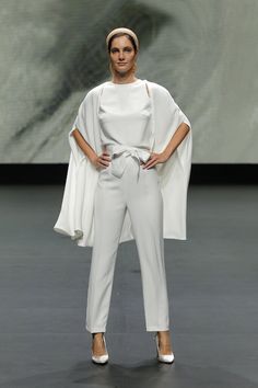 a woman is standing on the runway wearing white pants and a shawl over her head