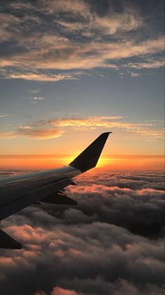 the wing of an airplane as it flies above the clouds at sunset or dawn in the sky