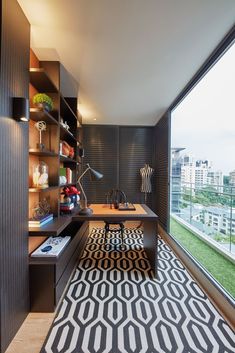 a room with a desk, shelves and a rug on the floor in front of a large window