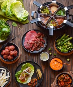 a table topped with plates and bowls filled with food next to utensils on top of a wooden table