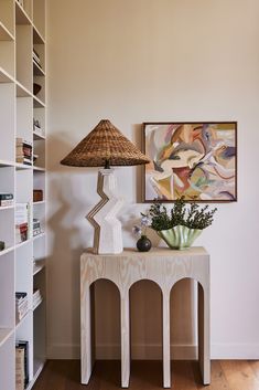 a white table with a lamp on top of it next to a book shelf filled with books