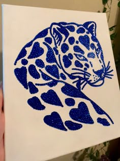 a hand holding up a blue and white paper with a drawing of a leopard on it