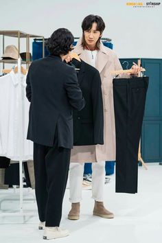 two people standing in front of a rack with clothes on it and one person looking at another