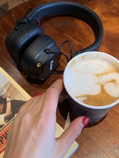 a woman's hand holding a cup of coffee with headphones on the table